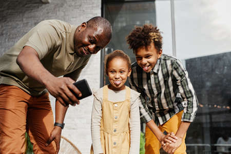 Portrait of smiling African-American man taking funny selfie with two kids outdoorsの写真素材