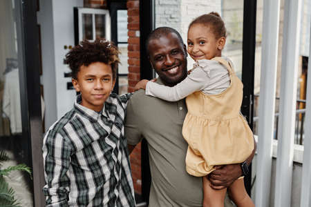 Portrait of proud African-American father posing with two children outdoors at terrace and looking at camera, copy spaceの写真素材