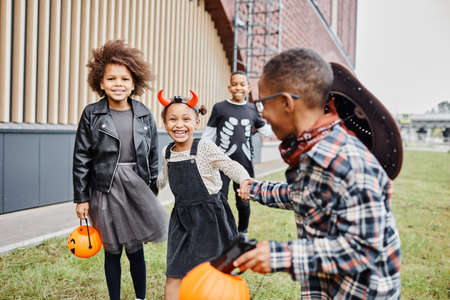 Group of cheerful African-American kids wearing Halloween costumes and running towards camera while trick or treating togetherの写真素材
