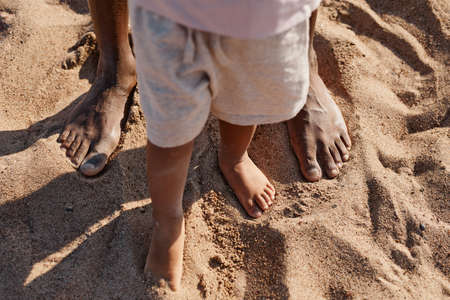 Top view of cute baby boy taking first steps while enjoying walk with dad on beach, copy spaceの写真素材