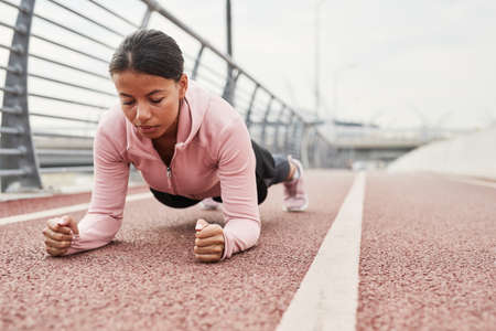 Young beautiful woman standing in the bar while training outdoors on the stadium