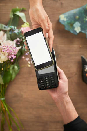 Top view close up of female customer paying via smartphone in flower shop, copy space