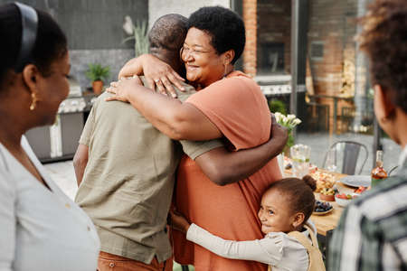Waist up portrait of mature African-American woman embracing friend during family gathering at dinner party outdoors, copy spaceの写真素材