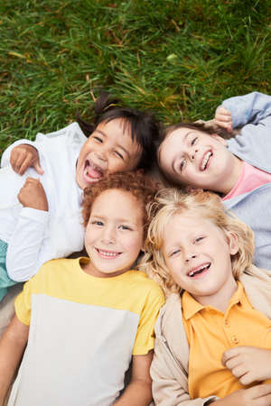 Vertical top view portrait of diverse group of kids lying on grass in park and looking at camera smilingの写真素材