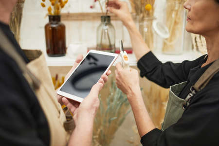 Close up of two mature florists using tablet while working in flower shop