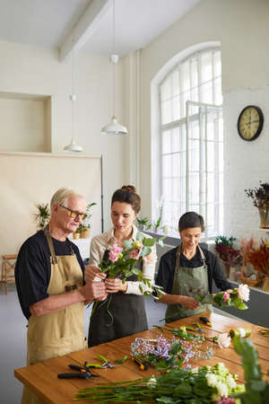 Vertical portrait of young female florist teaching mature couple arranging flower compositions in workshopの写真素材