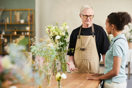 Waist up portrait of smiling senior man consulting young woman while working in flower shop, copy space, copy spaceの写真素材