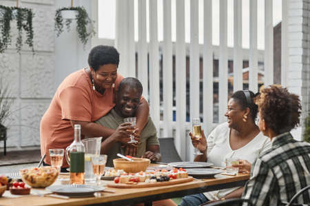 Portrait of two generation African-American family enjoying dinner together with senior couple embracing in foreground, copy spaceの写真素材