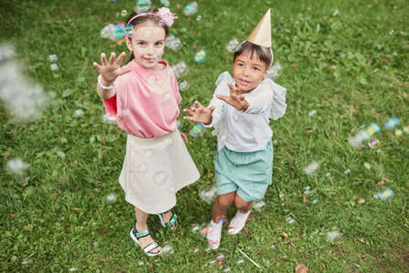 High angle portrait of two little girls playing with bubbles while enjoying Birthday party outdoors in Summerの写真素材