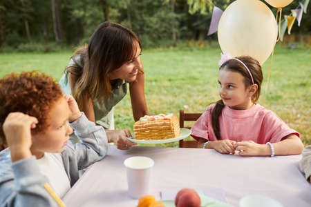 Portrait of smiling mother bringing Birthday cake to little girl during Birthday party outdoors, copy spaceの写真素材
