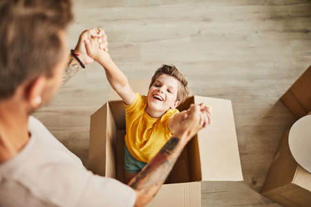 High angle view at father playing with cute boy in cardboard box while family moving to new house, copy spaceの写真素材