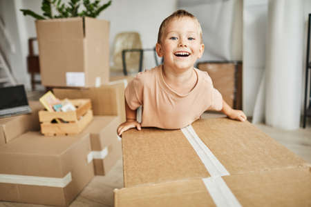 Portrait of cute happy boy moving boxes and playing while family relocating to new house, copy spaceの写真素材