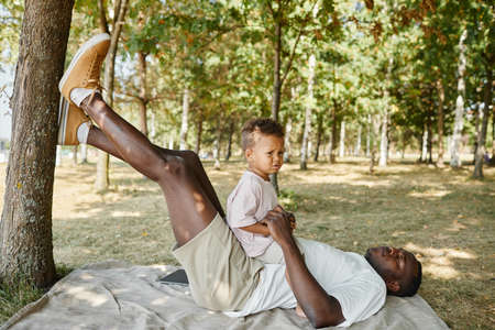 Full length side view portrait of African-American man playing with cute son in park, copy spaceの写真素材