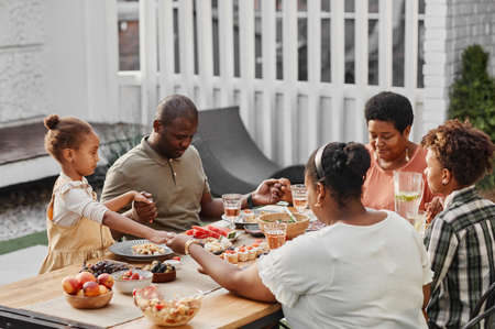 Portrait of big African-American family holding hands at dinner outdoors and praying, copy spaceの写真素材