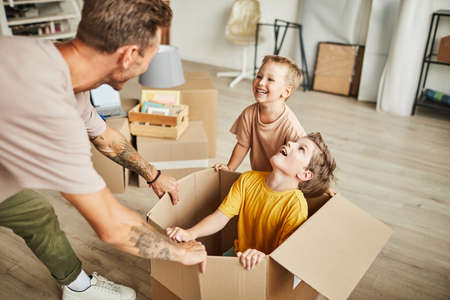 Portrait of happy father playing with two boys in cardboard boxes while family moving to new house, copy spaceの写真素材