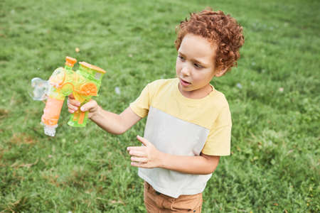 Portrait of curly boy playing with bubble toy outdoors in park, copy spaceの写真素材