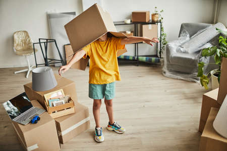Portrait of teenage boy with box on head playing with things while family moving to new house, copy spaceの写真素材