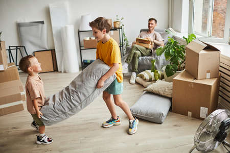 Portrait of two boys building pillow fort in room with boxes while family moving in to new house, copy spaceの写真素材