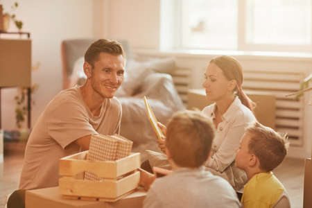 Portrait of happy family with two sons unpacking boxes in sunlight while moving in to new home, copy spaceの写真素材