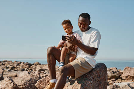 Portrait of smiling African-American father playing with cute son on beach, copy spaceの写真素材