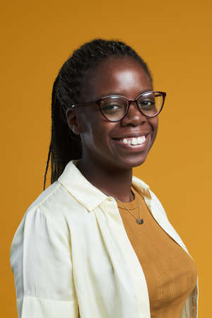 Vertical portrait of young African-American woman wearing glasses and smiling happily at camera...