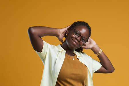 Portrait of carefree African-American woman looking at camera and smiling while posing against yellow background in studio, copy spaceの写真素材