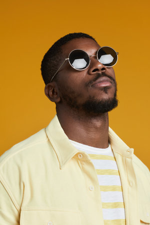 Vertical portrait of handsome African-American man wearing sunglasses while posing against yellow background in studioの写真素材