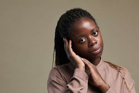 Minimal portrait of young African-American woman looking at camera gently smiling while posing against neutral brown beige background, copy spaceの写真素材