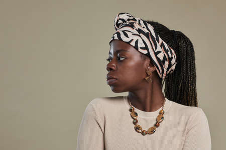 Minimal side view portrait of young African-American woman looking away while wearing ethnic accessories and posing against neutral brown beige background, copy spaceの写真素材