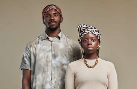 Waist up portrait of contemporary African-American couple wearing head wraps and looking at camera while standing against neutral beige background in studioの写真素材
