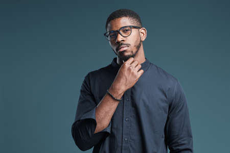 Waist up portrait of confident African-American man wearing glasses looking at camera while standing against deep blue background, copy spaceの写真素材