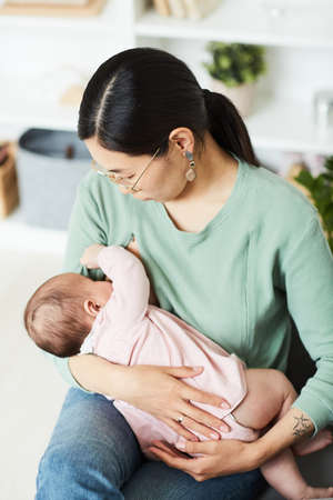 Young mother holding her baby on hands and feeding her before sleepingの写真素材
