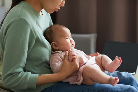 Young woman playing with her little daughter while she lying on her knees they sitting in the roomの写真素材