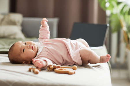 Little girl in pink body lying on the bed among the toys in the bedroomの写真素材