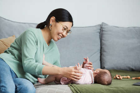 Happy Asian woman dressing her little daughter on the sofa in the roomの写真素材