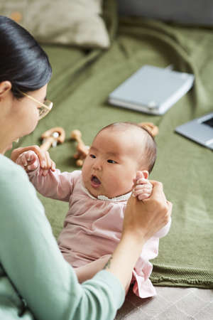 Rear view of young mother holding hands with her baby and developing her while awakeの写真素材