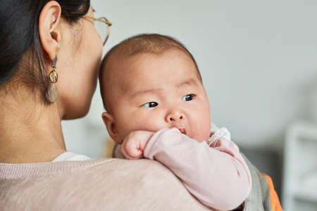 Rear view of young mother holding her little daughter on hands and caring about herの写真素材