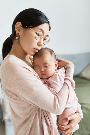 Asian young mother embracing her little daughter and loving her while she sleeping on her handsの写真素材