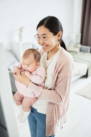 Asian woman holding her baby standing in the room and showing reflection in the mirrorの写真素材