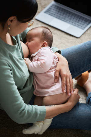 Young woman feeding her sleeping baby with breast sitting in the room