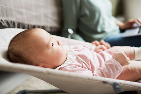 Close-up of newborn girl lying on lounge chair and looking away in the room