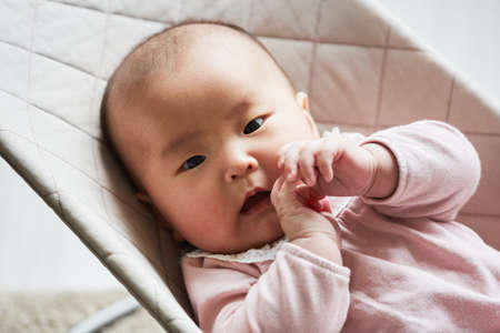 Close-up of Asian cute baby girl looking at camera while lying down on the bedの写真素材