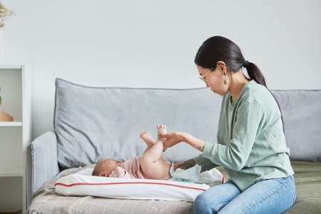 Young mother caring about the body of her baby before putting clothes on her while she lying on the bedの写真素材