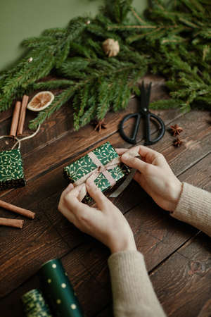 Close up of unrecognizable young woman wrapping Christmas gifts at rustic wooden table, copy spaceの写真素材