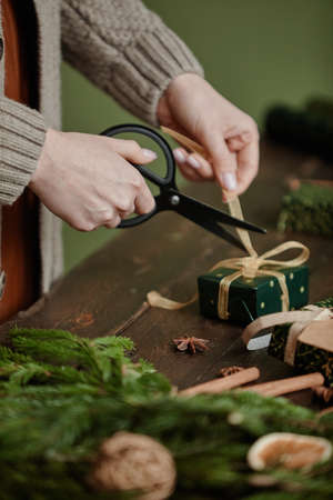 Close up of unrecognizable woman wrapping Christmas gifts at rustic wooden table, copy spaceの写真素材