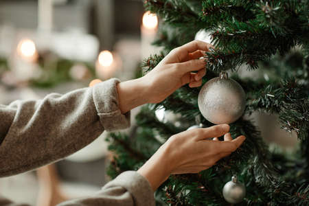 Side view close up of young woman decorating Christmas tree at home in elegant silver and grey tones, copy spaceの写真素材