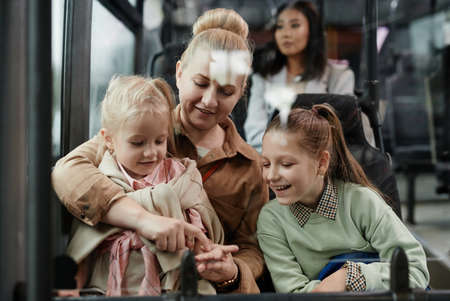 Portrait of adult woman with two kids having fun on bus while traveling by public transport in cityの写真素材