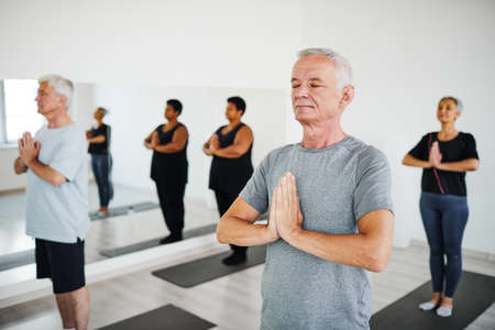 Group of senior people standing on mats with their eyes closed and meditating during training in gymの写真素材