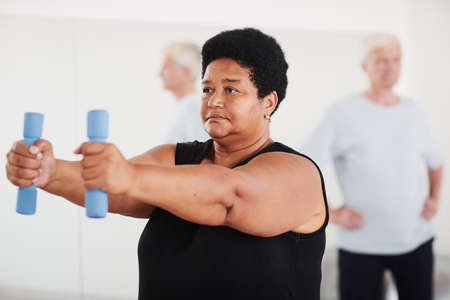 African mature woman doing sport exercises with dumbbells during training in the gym