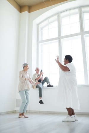 Two senior women dancing while friend shooting them on the mobile phone in dance studioの写真素材